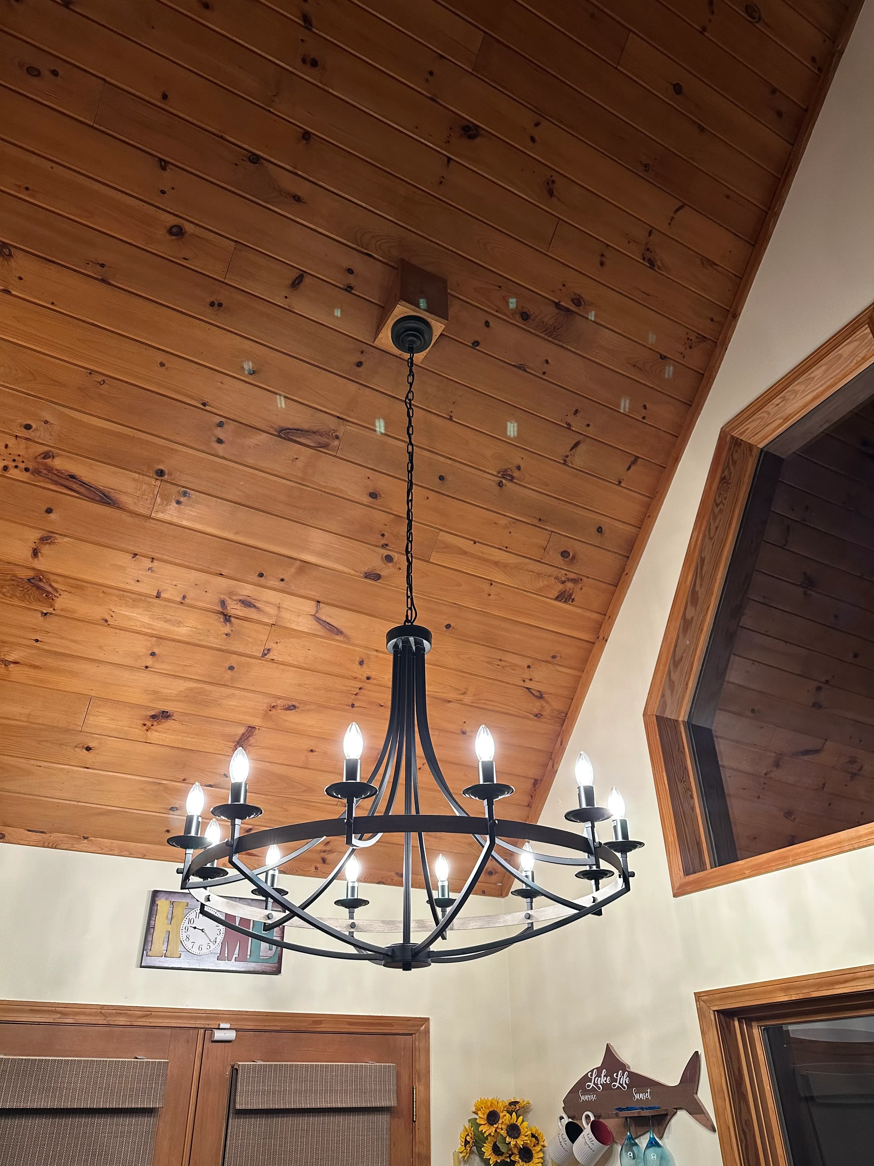 Large black circular chandelier illuminated beneath a wood-paneled vaulted ceiling