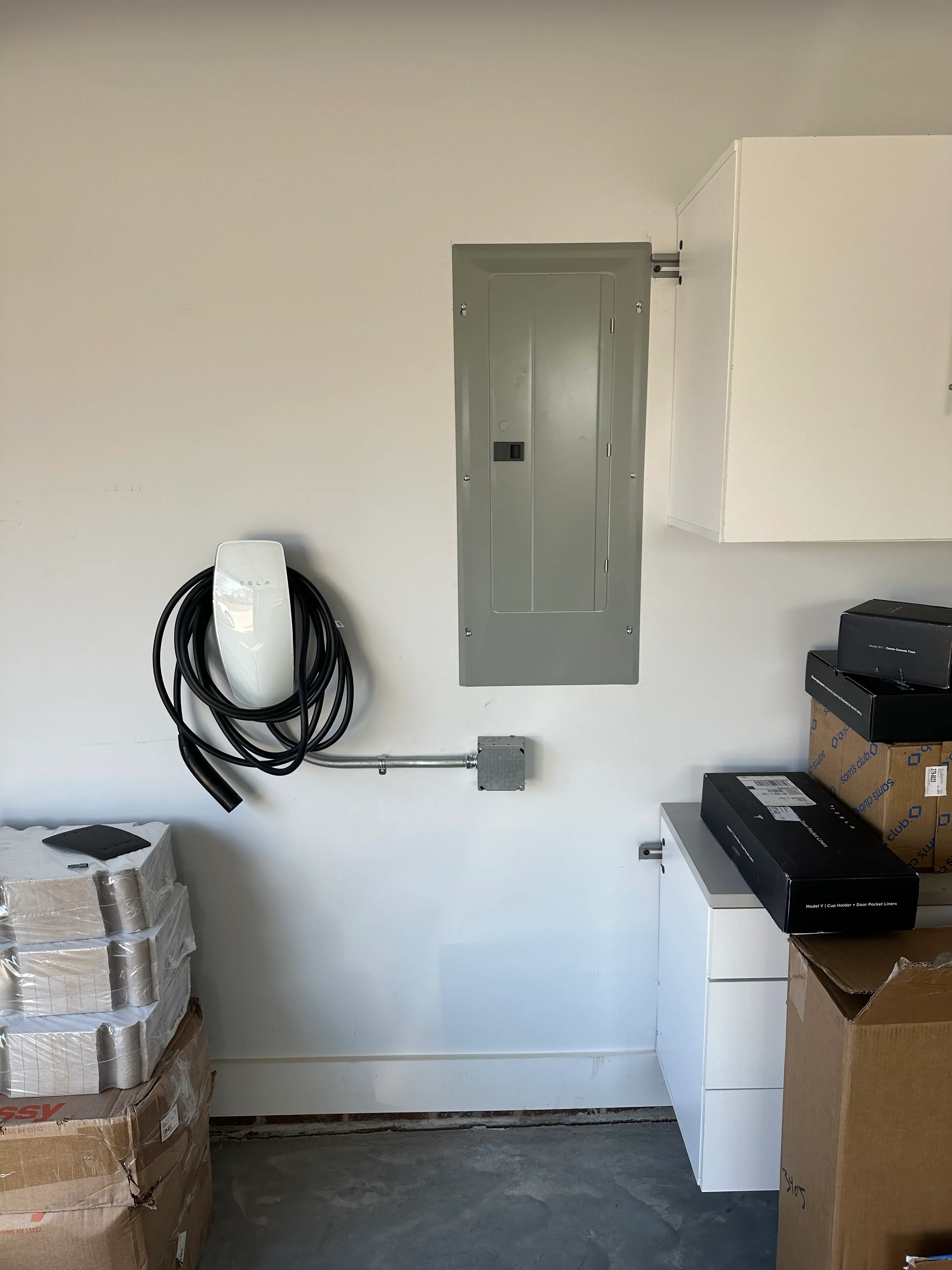 Wall-mounted white EV charger beside a gray electrical panel in a garage