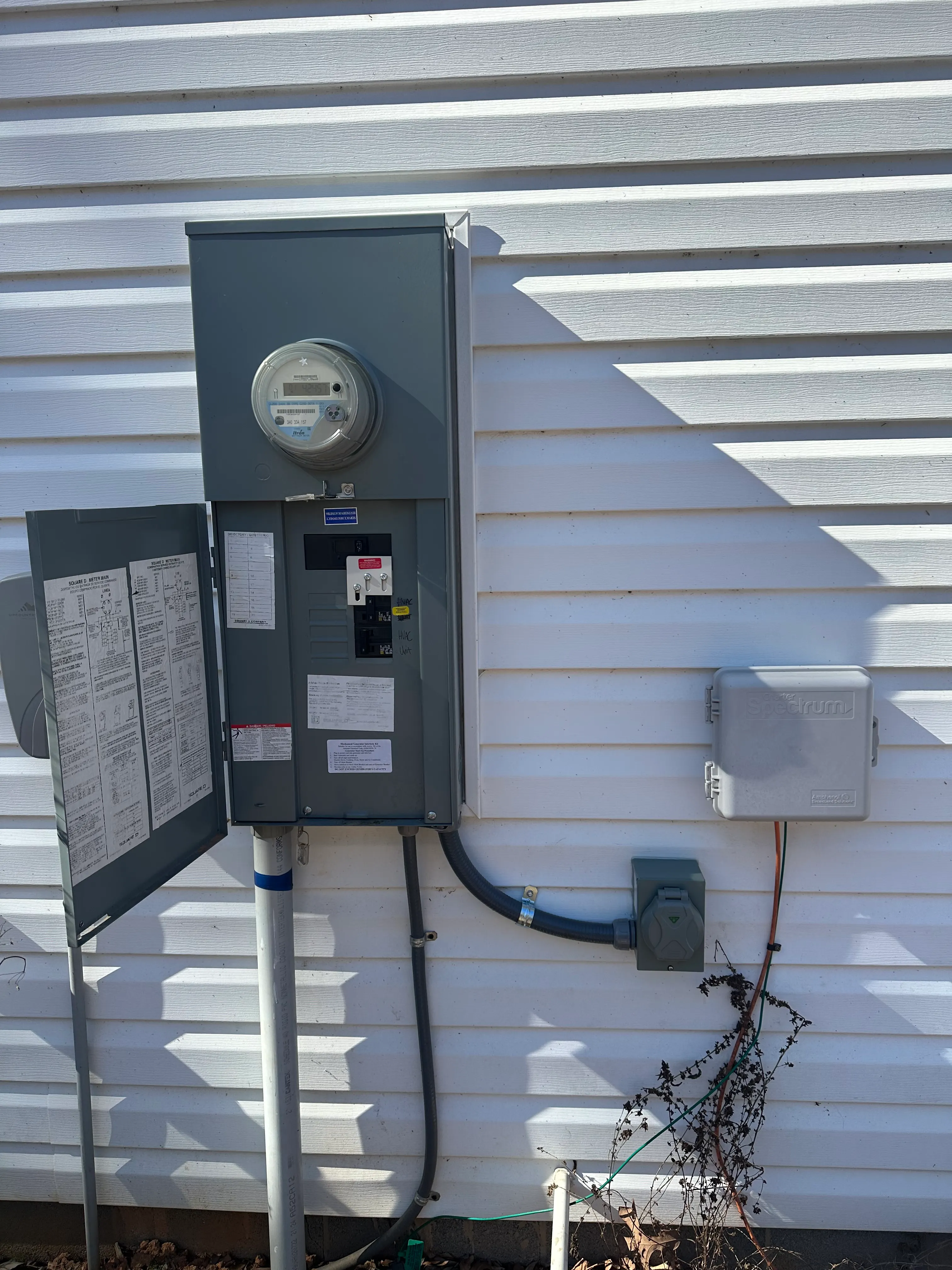 Open exterior electrical service panel and meter mounted on white siding